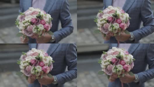新郎手捧婚礼花束站在街上。粉红色的衬衫，蓝色的夹克高清在线视频素材下载