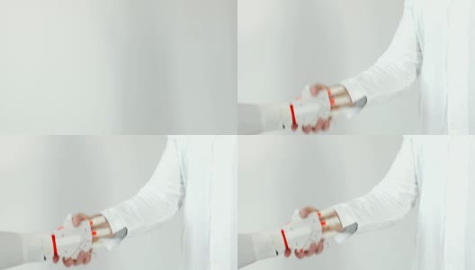 白色背景下穿白大褂的机器人假肢手与人的手握手高清在线视频素材下载