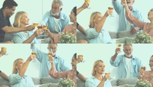 一群老年人在客厅聚会，喝着白葡萄酒，一起庆祝。白人，亚洲人，泰国人坐在家里的沙发上。退休生活方式的概念。高清在线视频素材下载