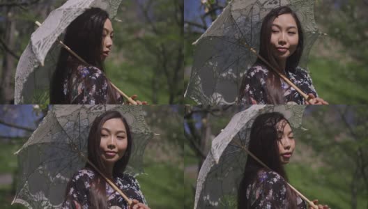 悠闲放松的亚洲妇女，带着白色太阳伞在阳光明媚的春天公园四处张望。自信苗条美丽的女士肖像享受户外阳光休闲。生活方式和休闲。高清在线视频素材下载
