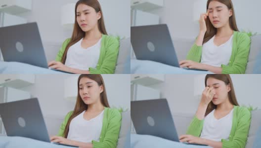 精疲力竭的亚洲女商人在使用笔记本电脑时伤了眼睛。年轻的女白领坐在沙发上感到视觉疲劳和眼睛疲劳，劳累劳累和按摩干燥易怒的眼睛在家里。高清在线视频素材下载