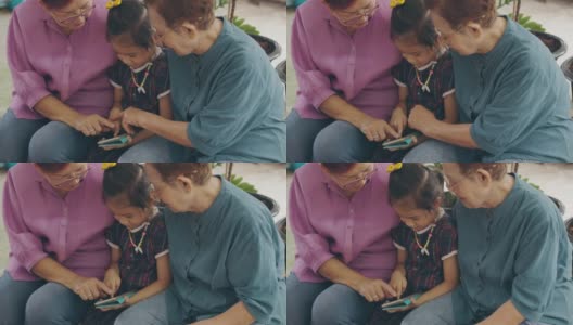 两位亚洲(泰国、中国)老奶奶和孙女一起玩智能手机，玩得很开心，体现了现代生活中利用互联网技术与人交流的理念。高清在线视频素材下载