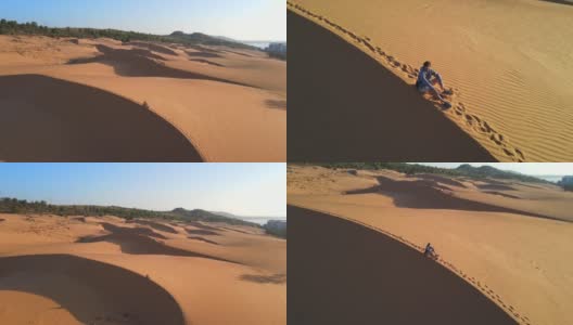 一名男子坐在沙漠中的沙丘上的航拍照片高清在线视频素材下载