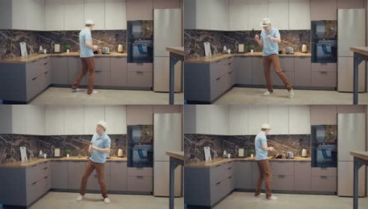 戴着帽子的年轻人在厨房里一边做饭一边跳舞唱歌，手里拿着勺子高清在线视频素材下载