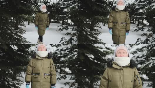 一个女孩在冬天里穿着暖和的冬装走在森林里，周围有许多树在雪地里高清在线视频素材下载