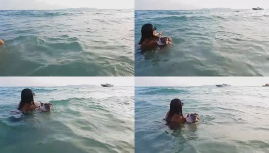 女人训练哈巴狗在海水里游泳，带着皮带和救生衣，有快艇和人在后面玩。高清在线视频素材下载