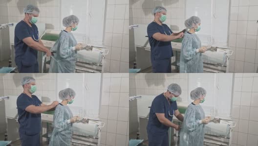 一队戴着口罩的医生正在为手术做准备。助手帮助外科医生穿上无菌的晨衣。医疗器械。健康理念，在医院工作。诊所设备高清在线视频素材下载