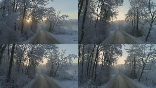 空中镜头:在雾濛濛的冬日夕阳下，通往令人毛骨悚然的白雪森林的空旷雾蒙蒙的道路高清在线视频素材下载