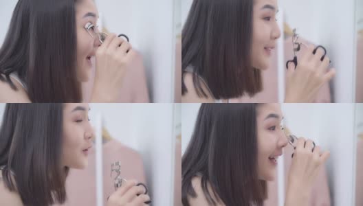 美丽的亚洲女人使用睫毛卷化妆前镜，快乐的女性使用美容化妆品提高自己准备在卧室在家里工作。生活方式女性在家放松的概念。高清在线视频素材下载