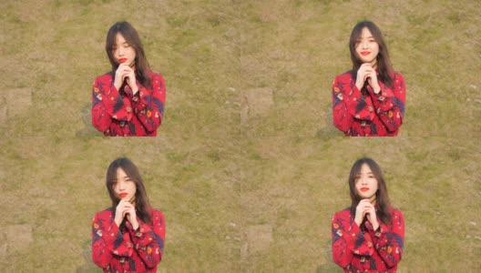 这是一幅美丽的中国年轻女子的肖像，她穿着红色的裙子看着镜头，以绿色的草地为背景做着祈祷的手势。高清在线视频素材下载