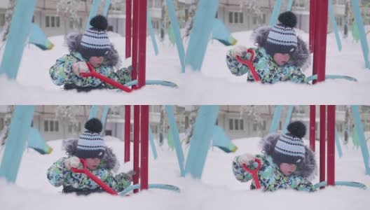 一个小孩在冬天的公园里玩雪。孩子拿着铁锹，在公园里积了很多雪。新鲜的空气里充满了乐趣和游戏。高清在线视频素材下载