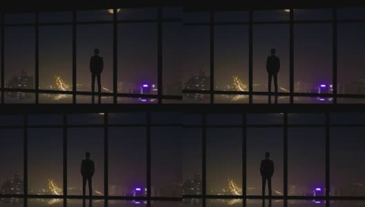 这名男子站在城市夜景的全景窗旁高清在线视频素材下载