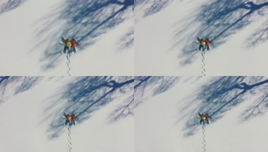 一对穿着彩色大衣的夫妇在厚厚的雪地上做蝴蝶的鸟瞰图高清在线视频素材下载