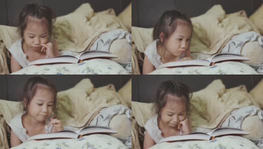 可爱的5岁亚洲女孩正在看书，躺在床上，有一盏灯发出美丽的黄色灯光。它是儿童学习、放松和发展创造力的睡前故事。高清在线视频素材下载