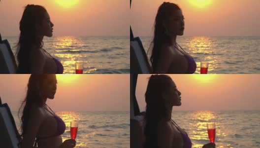 慢动作肖像美丽的亚洲女人在黑色比基尼和太阳镜享受与游艇在夏季日落饮酒。微笑性感女孩放松和享受奢侈的户外生活方式在暑假。高清在线视频素材下载
