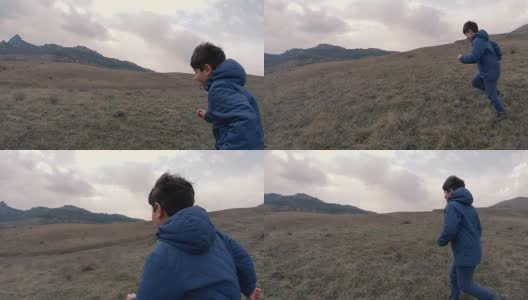 一个男孩在长着高草的场地上跑向群山环绕的地平线。慢动作视频高清在线视频素材下载