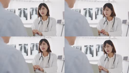 年轻的亚洲女医生正在用剪贴板传递好消息，谈论结果或症状与男性病人坐在健康诊所的桌子上。高清在线视频素材下载