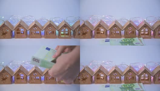 人们在清点欧元钞票，为买房付账。背景是木制的玩具房子——花环。购买和选择私人住宅的概念。现金付款。圣诞和新年，乔迁新居高清在线视频素材下载