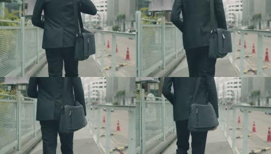 跟踪镜头:一名亚洲商人穿着休闲装，提着肩包走在大街上上班。高清在线视频素材下载