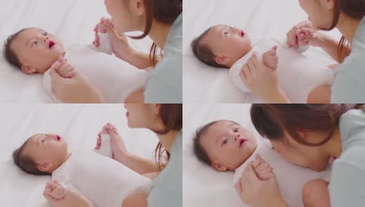 新亚洲妈妈玩可爱的新生婴儿在床上微笑和幸福在家里。妈妈和婴儿说话，牵着她的手一起笑。婴儿和母亲节的概念高清在线视频素材下载
