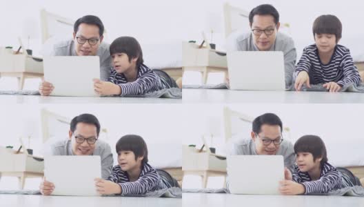 愉快的亚洲家庭一起在房间里度过时光。快乐的亚洲父亲和儿子躺在地毯上，在家里的卧室里使用笔记本电脑。高清在线视频素材下载