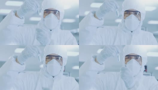 在实验室研究员/科学家穿着防护服拿着装有实验药物的试管并看着它。高清在线视频素材下载