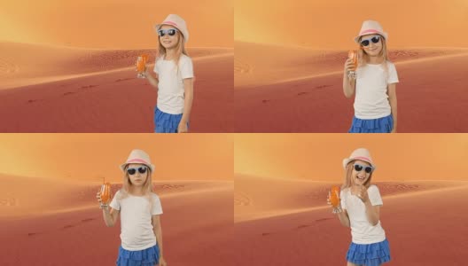 年轻的白人女孩喝橙汁。年轻女孩在撒哈拉沙漠感到口渴。沙漠气候非常炎热。夏天，在帽子里走着喝着新鲜的橙汁。高清在线视频素材下载