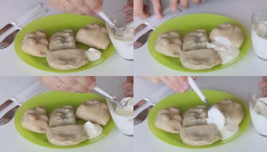 一个男人把酸奶油放在一盘现成的饺子上。高清在线视频素材下载