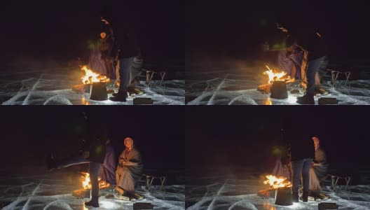 三个旅行者在夜间的冰面上着火。营地在冰上。帐篷紧挨着火。贝加尔湖。附近有一辆车。人们围着篝火取暖，穿着睡袋。高清在线视频素材下载