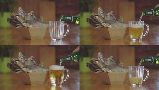 在干鱼面前把一瓶啤酒倒进玻璃杯里。木质吧台上放着一杯清凉的淡啤酒。小吃,啤酒。装干鱼的木碗。高清在线视频素材下载