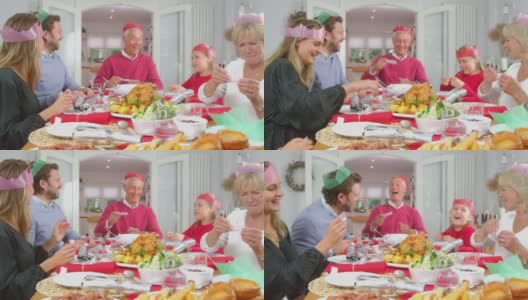一家人戴着纸帽子，带着圣诞饼干带来的礼物，坐在餐桌前一起吃饭高清在线视频素材下载