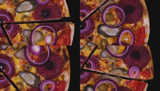 开胃的自制披萨，有意大利腊肠、泡菜、橄榄、西红柿、奶酪和洋葱圈，刚从烤箱中取出，切下来的一块在黑色背景上旋转高清在线视频素材下载
