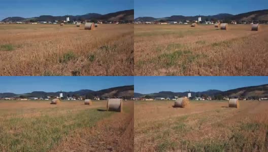 在有圆草堆的田野上空低空飞行。风景如画的小村庄和山峦为背景。高清在线视频素材下载