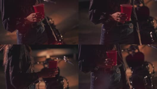 年轻的骑摩托车的女人拿着塑料杯在晚上的音乐节高清在线视频素材下载