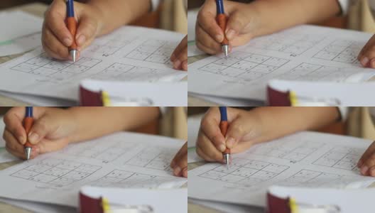 高级妇女的手试图解决数独谜与铅笔作为爱好在木制办公桌上。玩家将数字插入由9个方格组成的方格中，方格又细分为9个更小的方格。高清在线视频素材下载