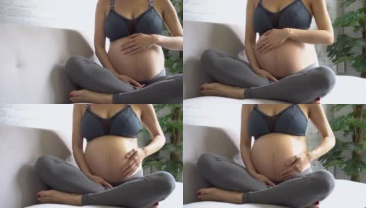 快乐的亚洲孕妇在运动服装触摸婴儿的肚子里高清在线视频素材下载