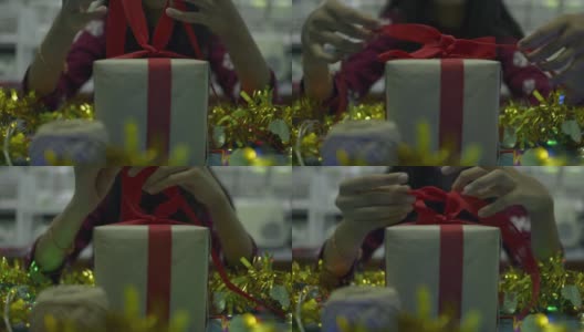 穿红衣服的女孩正在桌子上用红丝带系着蝴蝶结的礼品盒。为新年和圣诞节做准备。高清在线视频素材下载