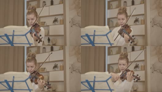 年轻的金发女人拉小提琴与音乐站在豪华的家庭内部高清在线视频素材下载