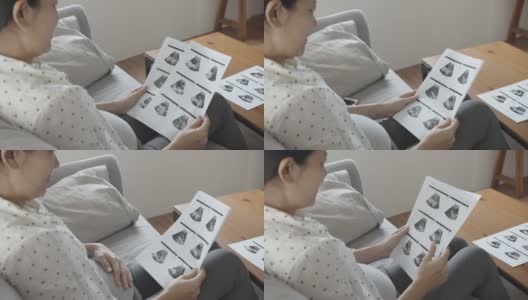 亚洲孕妇坐在沙发上看超声波图像。高清在线视频素材下载