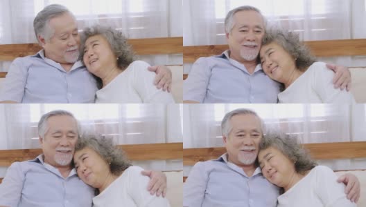 亚洲健康的爷爷坐在客厅的沙发上互相拥抱表示爱，欢快的老夫妇在房子里微笑高清在线视频素材下载