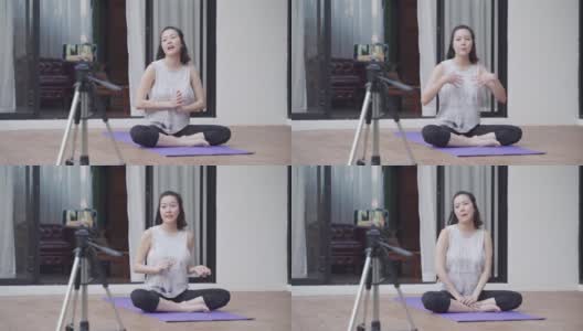亚洲女性在线教练瑜伽示范通过移动智能手机三脚架直播观众的姿势。女性健身辅导。教练与在家里在线教授瑜伽的学生交谈。高清在线视频素材下载