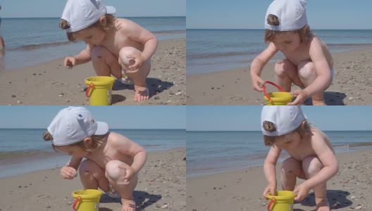 金发小男孩在海边玩耍。孩子在海边的沙滩上走着，玩着沙子和玩具。高清在线视频素材下载