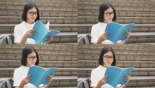 美丽的亚洲女学生坐在户外的肖像。女人拿着书与迷人的微笑相机。有教育观念的人。高清在线视频素材下载