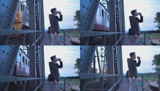 穿着大衣的亚洲游客在黑色铁桥铁路背景下喝着外卖咖啡杯。高清在线视频素材下载