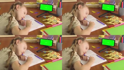 一个小女生正在桌子旁睡觉，她手里拿着一个绿色屏幕的智能手机。远程学习。高清在线视频素材下载