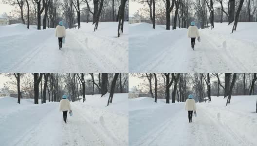 穿着白色毛皮大衣的漂亮女人在公园里散步。它正在下雪。缓慢的运动。冬季森林。时尚的女孩独自一人高清在线视频素材下载