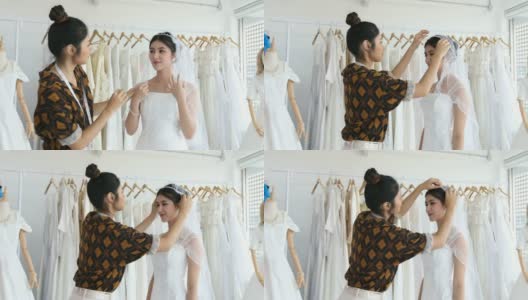 年轻美丽的亚洲新娘站在镜子前，试穿服装在工作室与时装设计师的婚礼在服装店高清在线视频素材下载
