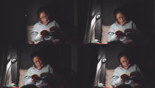 一个亚洲女人晚上在床上看书高清在线视频素材下载