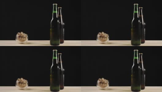 新鲜的啤酒。Hand拿着一碟开心果，旁边是绿色和棕色的瓶子，上面放着美味的精酿啤酒，放在一张黑色背景的木桌上。冰镇新鲜啤酒与水滴。4 k高清在线视频素材下载