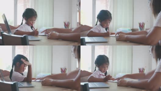 亚洲女童学生做她的家庭作业，而母亲在家工作。由于Covid - 19疫情，母亲教女儿做作业，他们在隔离期间呆在家里。高清在线视频素材下载